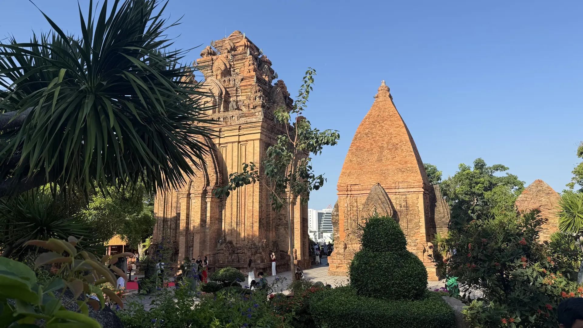 De bakstenen torens van het Po Nagar Cham-complex in Nha Trang, Vietnam, oranje aangelicht door de late middagzon boven de tropische tuinen eronder